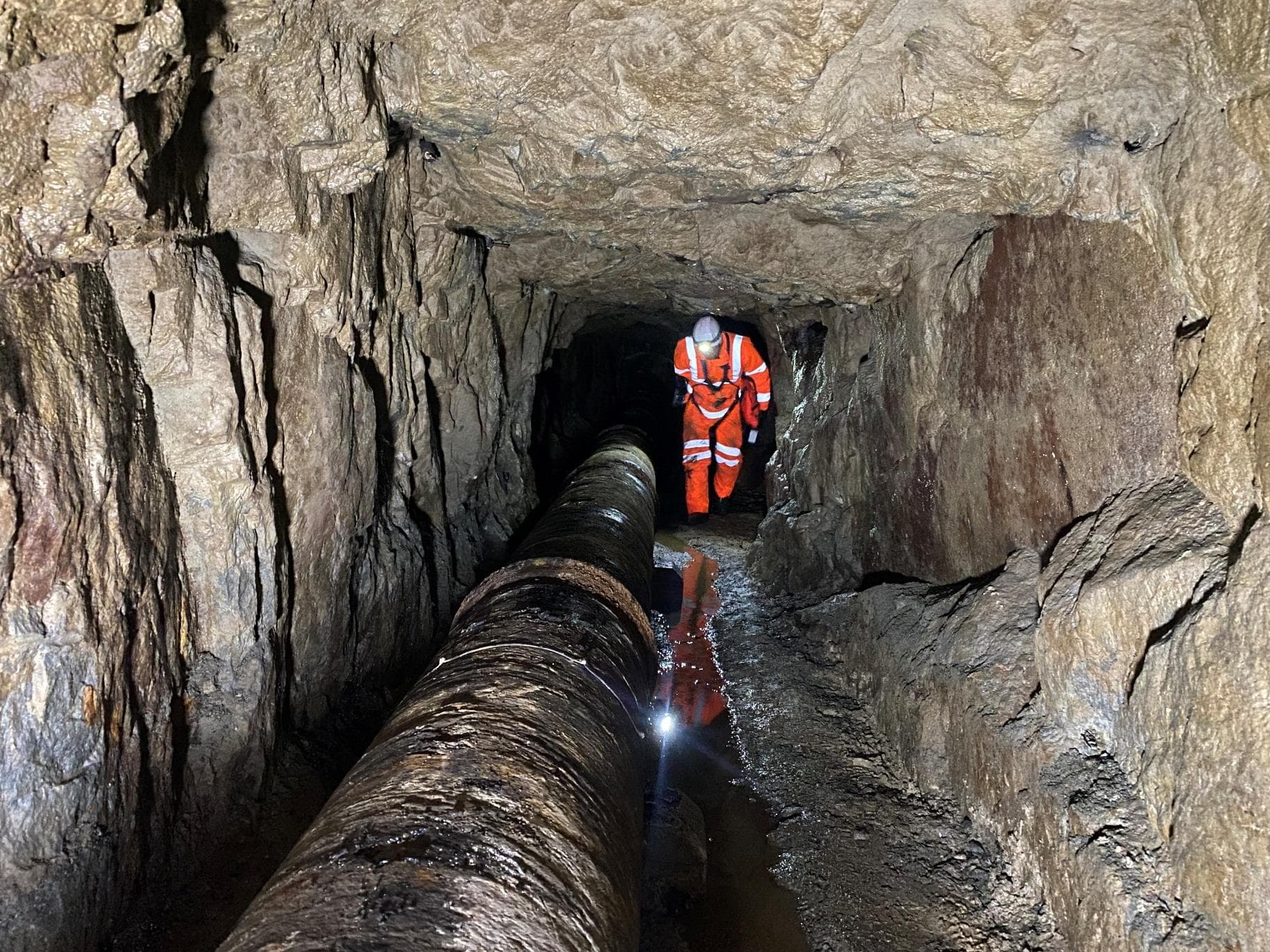 Inspector walking through a rock tunnel beside the corroded Dulyn Reservoir pipeline